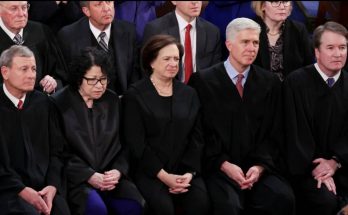Five Supreme Court justices in black robes seated in a row, with other officials