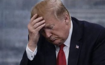 Man in dark suit and red tie holding his head with his hand