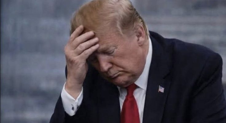 Man in dark suit and red tie holding his head with his hand