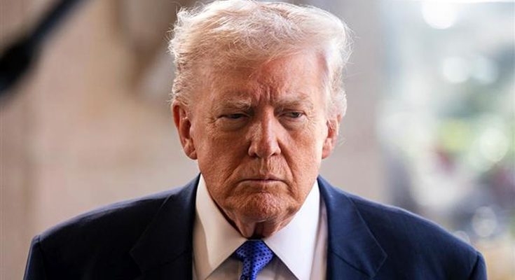 Close-up of a man with white hair wearing a dark suit and blue tie